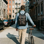 Black leather backpack worn on a city street with a bike