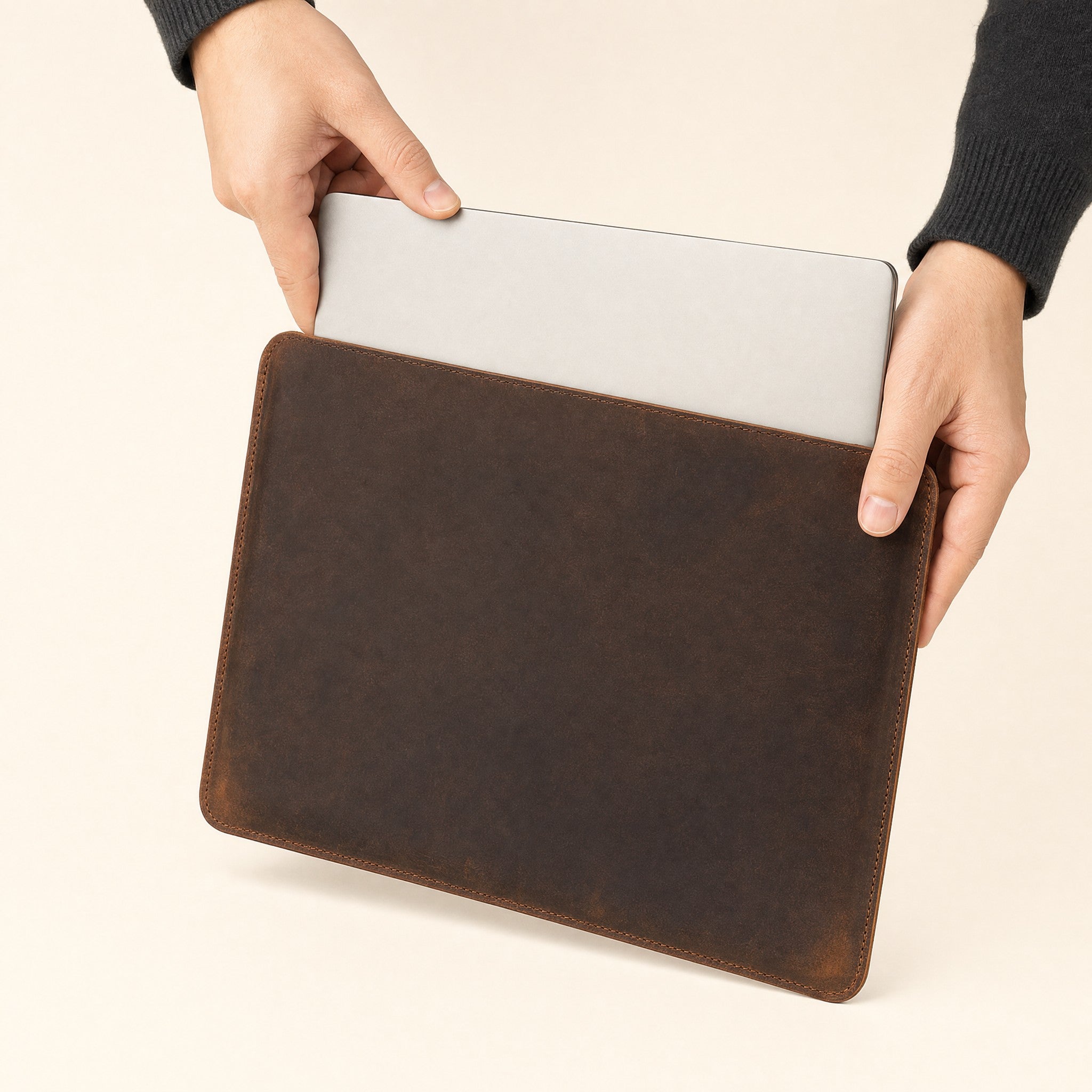 Hands sliding a laptop into the leather sleeve